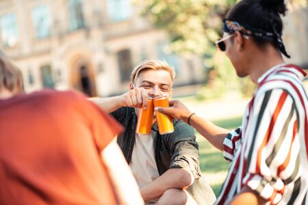 Waiting for holidays. Cheerful students clanging their pop cans celebrating the end of the academic year on picnic.の写真素材
