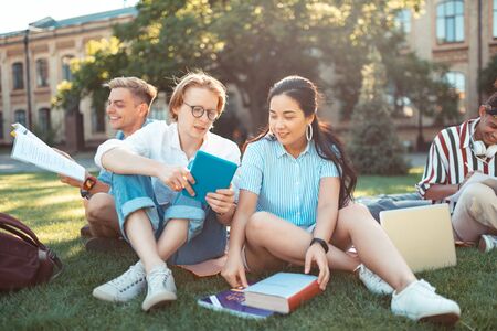 Graduating students. Group of concentrated young people studying and doing homework sitting on the grass lawn in front of their university.の写真素材