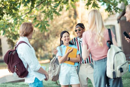Joking around after classes. Group of students standing together in the university yard joking and...