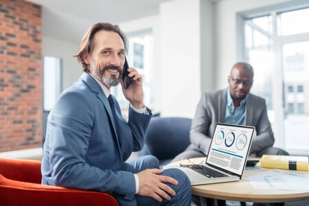 Businessman smiling. Grey-haired bearded businessman smiling while receiving call from colleague