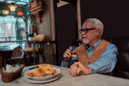Salad and whisky. Grey-haired bearded man eating salad and drinking whisky alone in the restaurantの写真素材