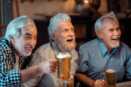 Pensioners laughing. Three pensioners laughing while watching football in pub and drinking beerの写真素材