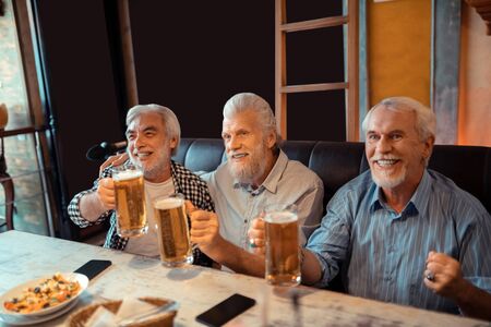 Pensioners feeling happy. Beaming pensioners feeling happy while drinking beer and watching footballの写真素材