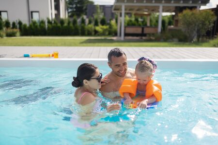 Happy parents. Happy good-looking parents feeling unbelievable swimming in pool with daughterの写真素材