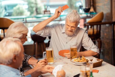 Pensioners playing cards. Grey-haired positive pensioners playing cards and drinkingの写真素材