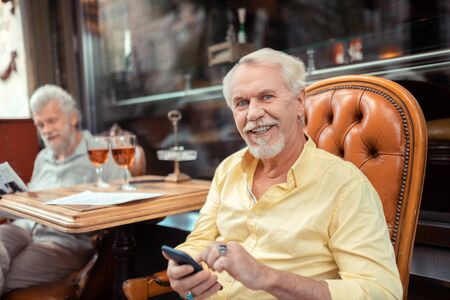 Blue-eyed man. Blue-eyed retired man holding smartphone while spending time with friendの写真素材