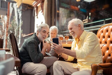 Showing photos. Bearded man wearing yellow shirt showing photos to his old friendの写真素材