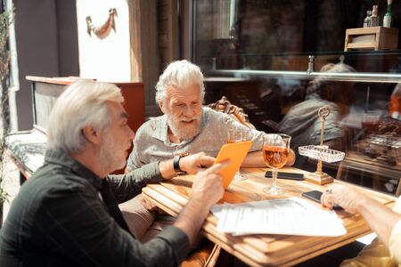 Men using tablet. Bearded men using tablet while talking and drinking outside at the weekendの写真素材