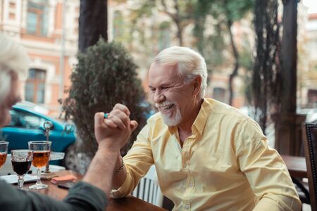 Man winning. Bearded grey-haired man laughing while winning at arm-wrestlingの写真素材