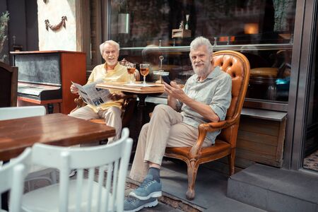 Enjoying time outside. Retired men reading news and enjoying time outside while sitting near cafeteriaの写真素材