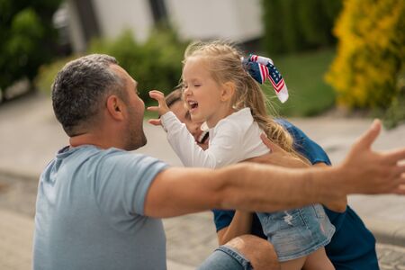 Making funny face. Cute blonde girl making funny face while hugging parents standing outside