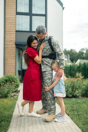 Strong heroic husband. Dark-haired wife wearing red dress standing near her strong heroic husband and daughterの写真素材