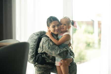 Hugging lovely girl. Mature military woman wearing backpack hugging her lovely beautiful girlの写真素材