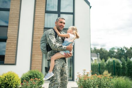 Standing near house. Serviceman in uniform feeling amazing standing near house with daughterの写真素材