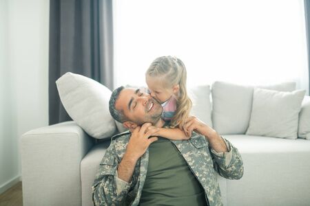 Loving daughter kissing. Cheerful and cute loving daughter kissing her father being hero for the familyの写真素材