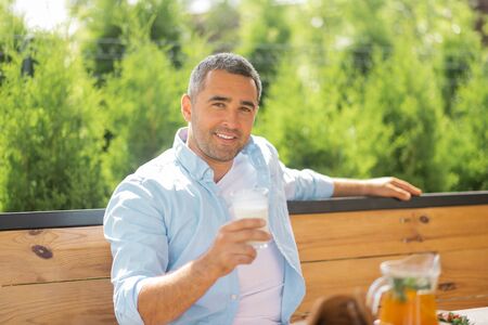 Handsome man smiling. Handsome man smiling while having early meal outside on summer terraceの写真素材