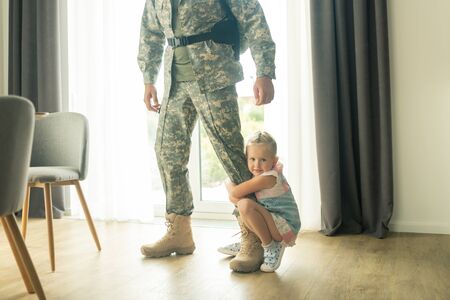 Hugging father leg. Little blonde girl hugging her father leg while he leaving house for military serviceの写真素材