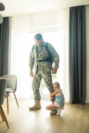 Saying goodbye. Man leaving home for military service saying goodbye to little emotional daughterの写真素材