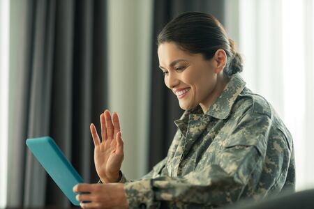 Beaming woman. Beaming woman serving in armed forces waving while having video chat with childrenの写真素材