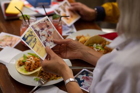 Happy memories. Woman holding in hands two photographs from her holiday looking at them during her lunch.の写真素材