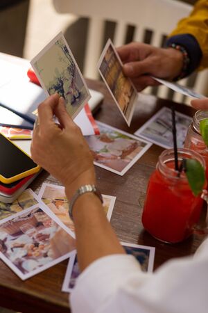 Printed memories. Married couple looking at their old photographs from past travels holding them in...