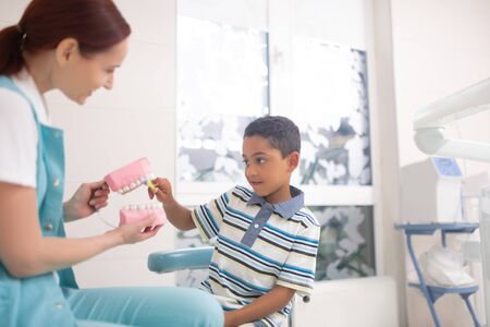 Cute dark-skinned boy. Cute dark-skinned boy using tooth brush on teeth model sitting near child...