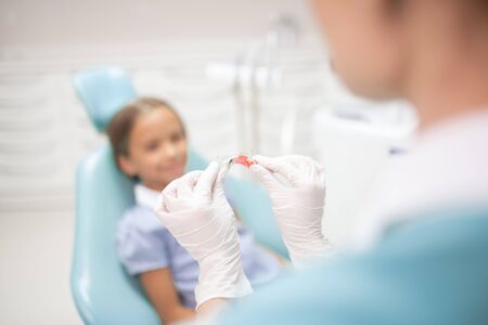 Showing mouth guard. Close up of child dentist wearing white gloves showing mouth guard to girl