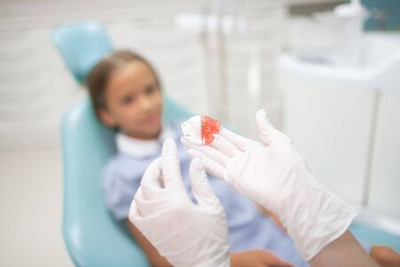 Wearing white gloves. Close up of child dentist wearing white gloves holding night guard for girl