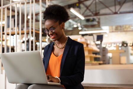 Office worker. Beautiful stylish African-American office worker using laptop while working hardの写真素材