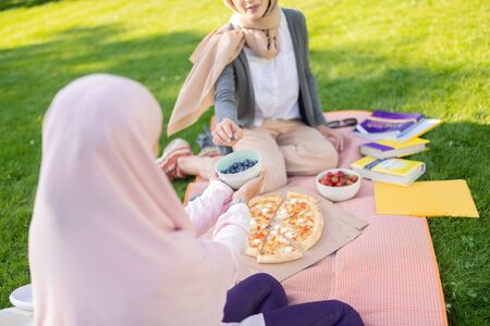 Blueberries after studying. Women in hijab taking blueberries after studying with friend outsideの写真素材