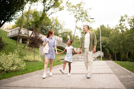 Talking to daughter. Adoptive parents talking to their cute lovely daughter while walking in the parkの写真素材