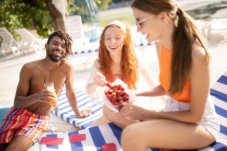 Sharing strawberries. Beautiful woman sharing strawberries with friends while resting near river