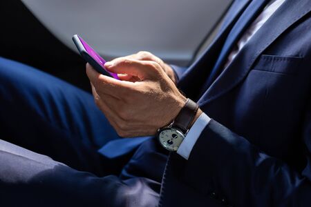 Texting friend. Close up of businessman wearing hand watch texting friend using smartphoneの写真素材