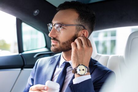 Man taking headphones. Bearded man wearing glasses taking headphones while sitting in his car