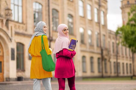 Student holding books. Smiling muslim student holding books walking to classes with friendの写真素材