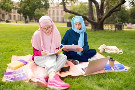 Muslim woman. Close up of dark-eyed muslim woman wearing hijab sitting outside with friendの写真素材