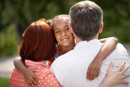 Hugging parents. Dark-skinned appealing cute girl hugging foster parents while meeting themの写真素材