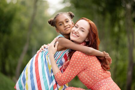 Mother hugging. Loving caring red-haired mother hugging her cute appealing daughterの写真素材