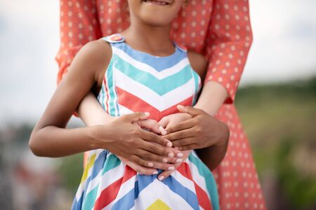 Hands of mother. Close up of dark-skinned girl wearing bright dress touching hands of motherの写真素材