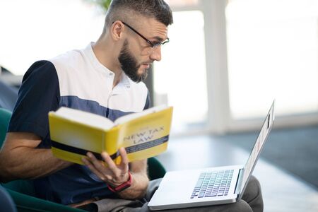 Laptop and book. Promising smart businessman holding laptop and book while studying taw law