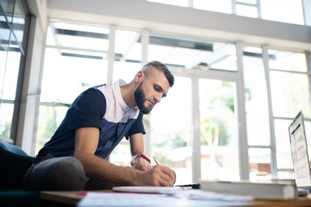 Businessman noting down. Busy young businessman noting down some statements while working hard