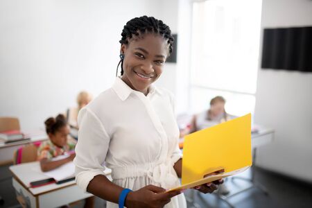 Cheerful teacher. Cheerful dark-skinned teacher wearing white blouse feeling good at workの写真素材