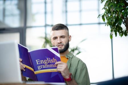 Studying English grammar. Bearded young businessman sitting in spacious office and studying English grammarの写真素材