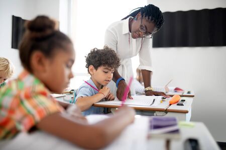 Curly boy listening. Curly dark-haired boy listening to African-American teacher wearing glasses