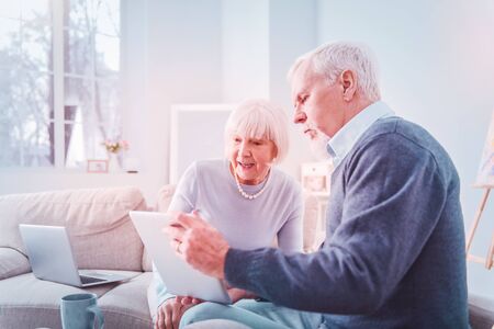 Grey-haired pensioner. Grey-haired pensioner wearing dark blue sweater showing photos on tablet his...
