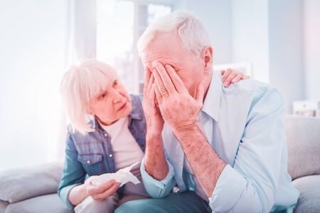 Worried woman. Beautiful blonde-haired woman feeling worried about health of her bearded grey-haired manの写真素材