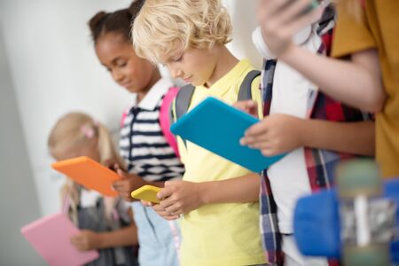 Addicted to gadgets. Children addicted to gadgets playing games in school corridor while standing...