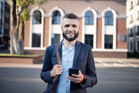 Man standing outside. Businessman wearing smart watch holding smartphone while standing outsideの写真素材