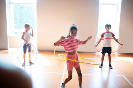 Girl feeling amazing. Dark-skinned girl wearing pink shorts feeling amazing while rolling hula-hoop