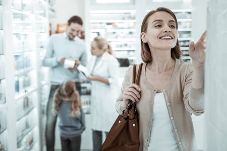 Advices of druggist. A twinkly charming woman selecting the pills blister while the nice pharmacologist with blonde pony-tail and white coat advising her dark-haired handsome husband and sweet kid.の写真素材